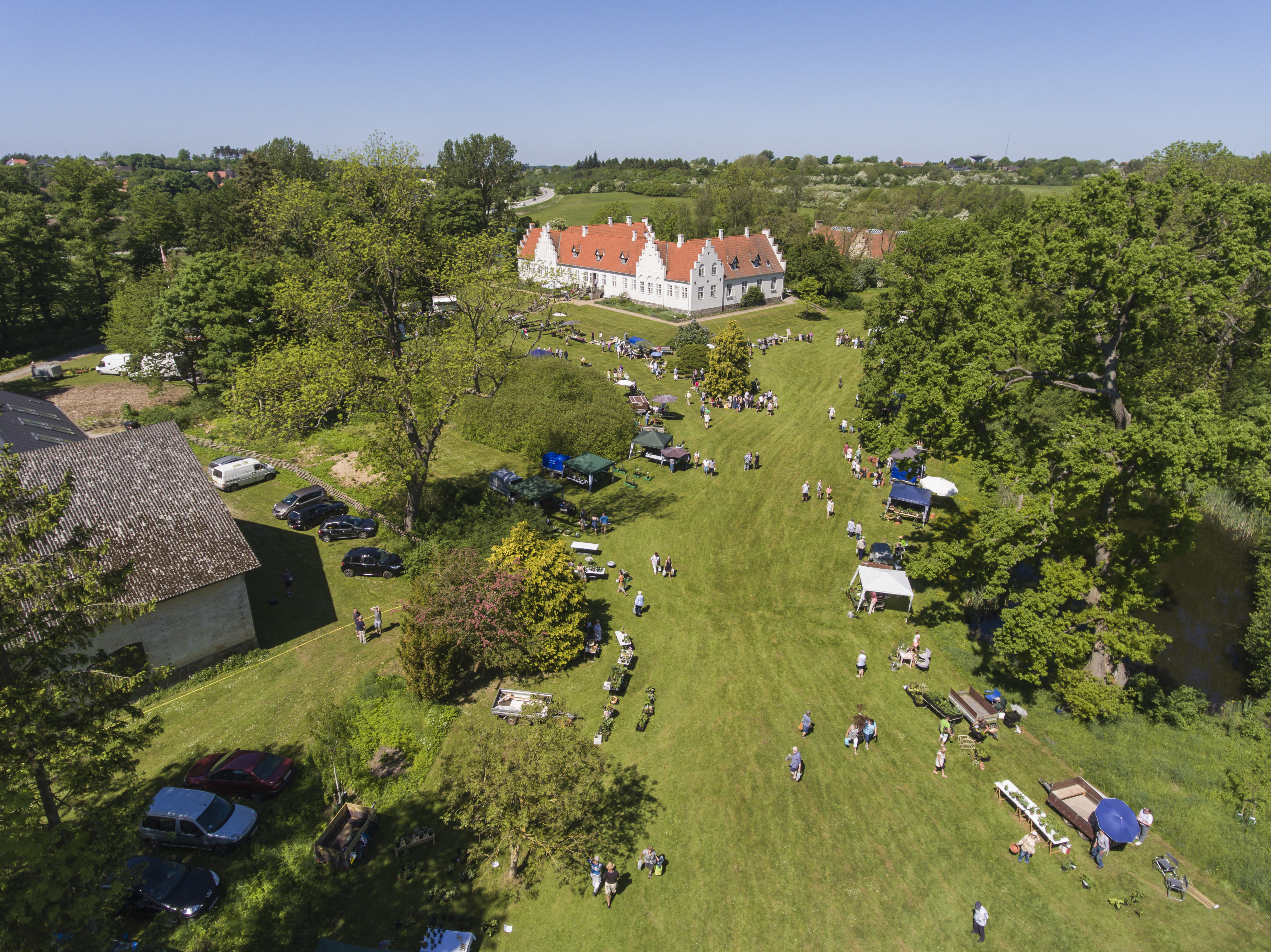 Hvid bygning på græsplæne med omkringliggende træer en sommerdag